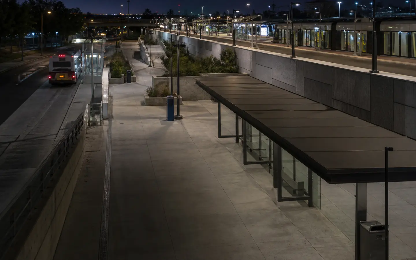 Layered bus and rail platforms connected by empty paths at a fictional evening transit interchange