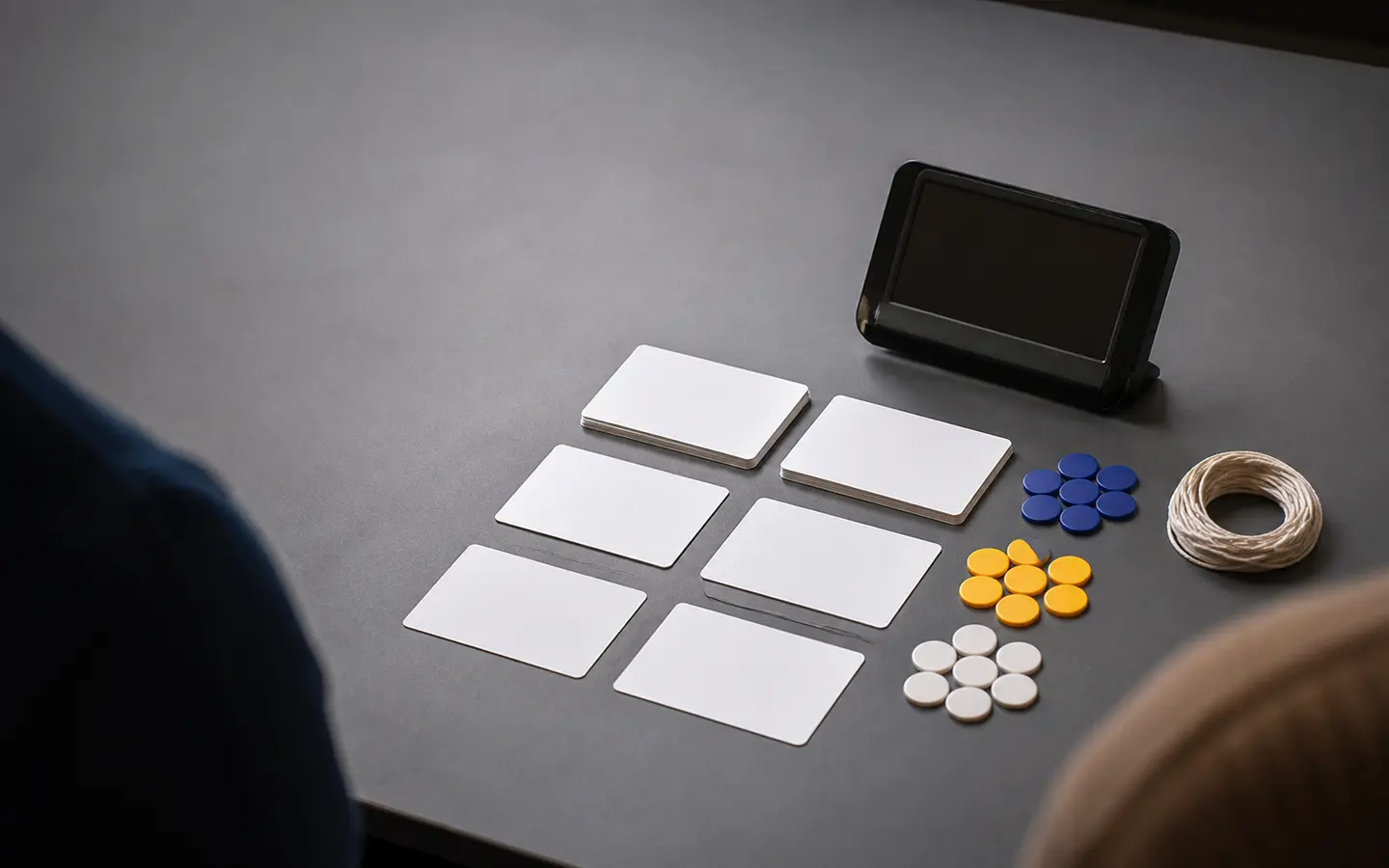 Blank transit research cards, colored tokens, string, and a dark-screen device between two partial participant shoulders