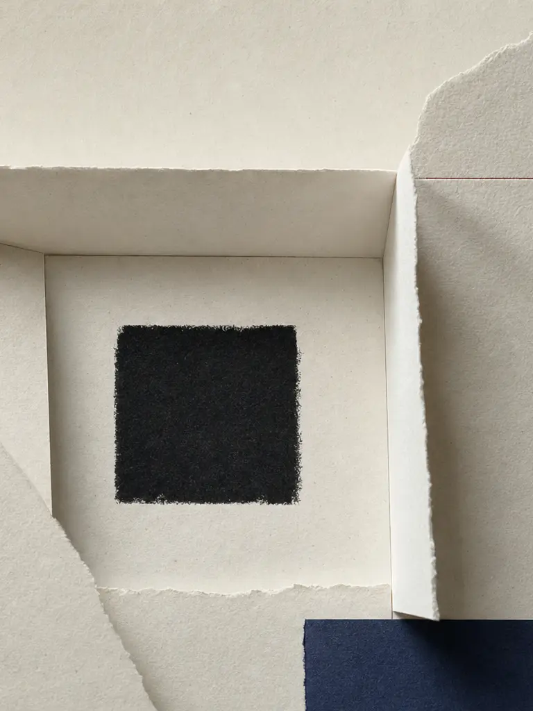 Folded ivory paper frame surrounding a black square beside a red field. Portrait crop.