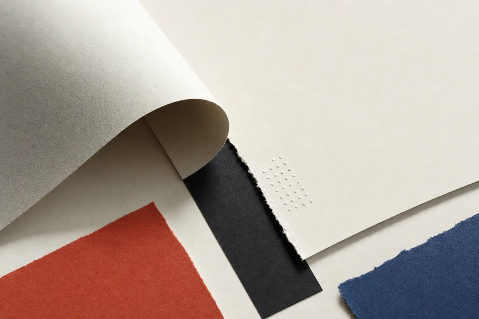Curled ivory sheet above black, red, and blue paper fragments.